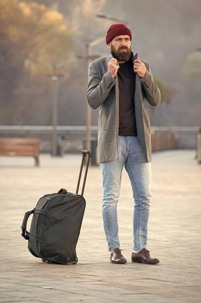 Looking for accommodation. Man bearded hipster travel with big luggage bag wait for taxi bring him to hotel. Travel tips. Traveler with suitcase arrive travel destination. Hipster ready enjoy travel