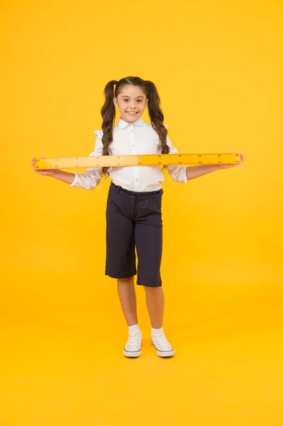 Μήκος μέτρησης. Κοριτσάκι με μετρικό χάρακα σε κίτρινο φόντο. Μικρό κορίτσι ετοιμάζεται για μαθηματικά και μάθημα γεωμετρίας. Χαριτωμένο κορίτσι χαμογελά με όργανο μέτρησης. Ευτυχισμένο κορίτσι είναι πίσω στο σχολείο — Φωτογραφία Αρχείου