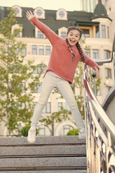 Běžel ze schodů. Šťastné energické dítě skákající po schodech v neformálním oblečení. Energická holčička s dlouhými copánky v pohybu. Energické malé dítě se usmívá ve vzduchu. Aktivní a energické — Stock fotografie