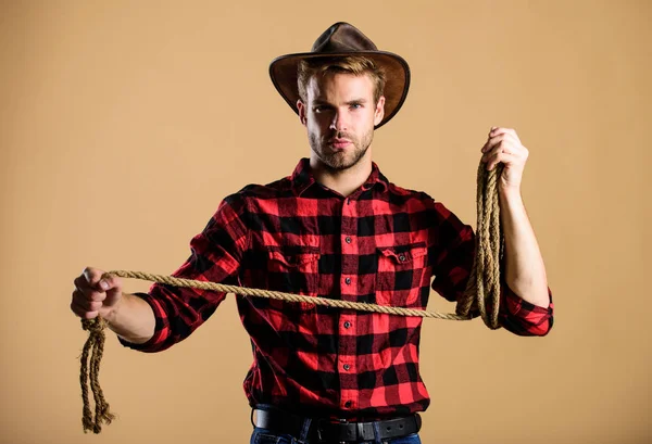 Lasso tool of American cowboy. Ranch occupations. Lasso is used in rodeos part competitive events. Lasso can be tied or wrapped. Western life. Man cowboy beige background. Man wearing hat hold rope — стокове фото