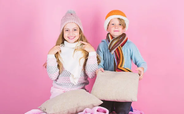 Děti chlapec a dívka zahřívací polštáře a klobouky. Zůstaňte v teple a pohodlí. Zimní oblečení s roztomilé a příjemné doplňky pro zahřátí. Sourozenci nosit zimní teplá čepice sedět na růžovém pozadí — Stock fotografie