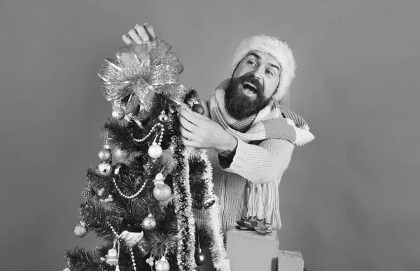 Man with beard and tricky smile puts bow on tree — Stock Photo, Image