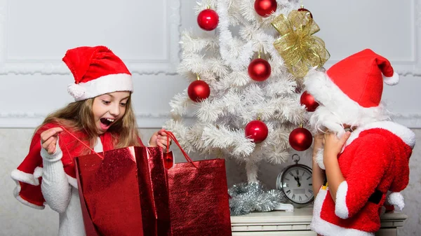 Desempaquetar regalos de Navidad. Razón por la que los niños aman la Navidad. Los niños celebran la Navidad con regalos. Niño niño santa con barba artificial blanca y sombrero rojo dan bolsa a la chica. Papá Noel trae regalo de Navidad —  Fotos de Stock