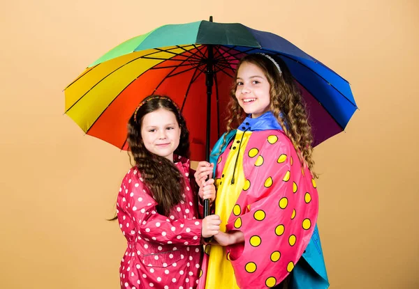 Il est plus facile d'être heureux ensemble. Sois arc-en-ciel dans certains nuages. Amusant jour de pluie. Bonne promenade sous le parapluie. Les enfants filles heureux amis sous parapluie. Météo pluvieuse avec des vêtements appropriés. Parapluie lumineux — Photo