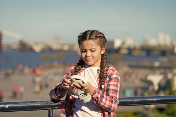 Menina criança segurar fones de ouvido dobráveis enquanto caminham ao ar livre. Dispositivo de música moderna. Benefícios dos fones de ouvido dobráveis. Dobrabilidade torna mais portátil. Melhores fones de ouvido dobráveis e portáteis — Fotografia de Stock