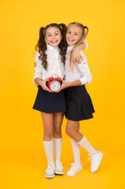 Okul sabah meydan okuma geri evcilleştirme. Küçük okul çocukları sarı arka plan üzerinde sabah sınıfları önce gülümseyen. Mutlu küçük kızlar sabahın erken saatlerinde saat tutan. Okul için sabah rutini