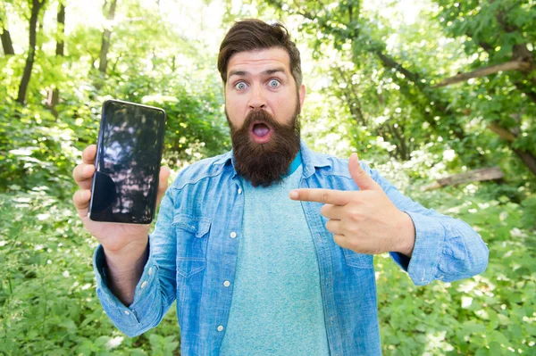 oh my god. surprised bearded man pointing finger on phone. Mature hipster with beard. got lost in forest. brutal man with phone. hipster style. guy in forest use gps navigation. summer camping