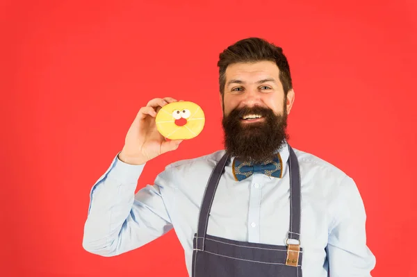 Щасливий пекар. Бородатий пекар тримає пончик на червоному тлі. Випічка печива в пекарні. Слідуючи улюбленому рецепту випічки — стокове фото