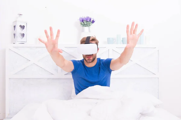 Virtual reality lets you travel without leaving the room. Handsome man using virtual reality device in bedroom. Caucasian guy wearing virtual reality headset in bed. Simulating virtual reality