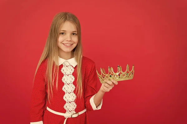 Найкраща нагорода для мене. Малюк тримає золоту корону символ принцеси. Щаслива концепція дитинства. Кожна дівчина, яка мріє стати принцесою. Пані маленька принцеса. Дівчина мила посмішка тримає корону, стоячи на червоному тлі — стокове фото