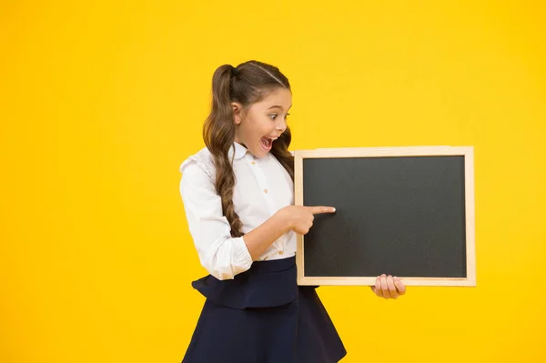 Een goede publiciteit voor onze school. Kleine Kid wijzende vinger op blanco Blackboard met school publiciteit. Klein kind toont publiciteit evenement op opgeruimd leeg schoolbord. Reclamebord, kopieer ruimte — Stockfoto