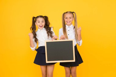 Bilgi vermek. Küçük çocuklar sarı arka plan hakkında bilgi için boş tahta ile evet jest yapıyor. Düzenli bilgi panosu olan küçük kız öğrenciler. Mutlu bilgileri paylaşma, kopyalama alanı