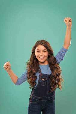 Tatlı kız uzun kıvırcık saçlı, mutlu, gülümseyen. Çocuk psikolojisi ve gelişimi. Mutlu galip. Zaferi ya da başarıyı kutlayın. Başarılı mutlu çocuk. Başarıya ulaş. Neşeli çocuk zaferi kutluyor