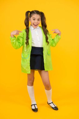 Yağmurlu bir günde çocuğunuzu korumak. Mutlu çocuk sarı arka plan üzerinde yağmur panço işaret. Küçük çocuk sonbaharda okula dönüyor. Okul üniforması uzun esmer saçlı gülümseyen küçük çocuk