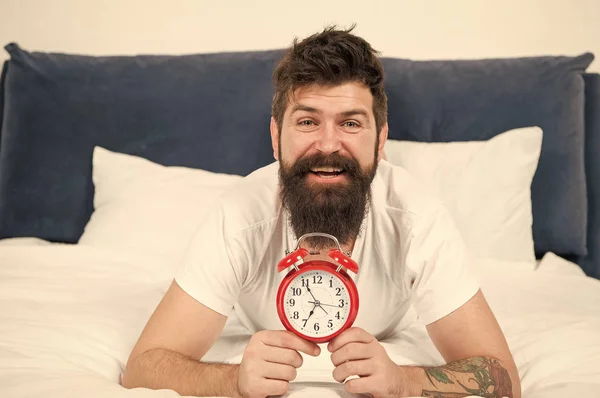 Lucky to start the day here. brutal sleepy man in bedroom. mature male with beard in pajama on bed. asleep and awake. energy and tiredness. time management. happy bearded man hipster with alarm clock