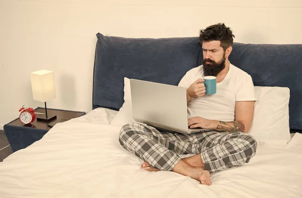 Just woke up and already at work. Hipster bearded guy pajamas freelance worker. Remote work concept. Social networks internet addiction. Online shopping. Man surfing internet or work online