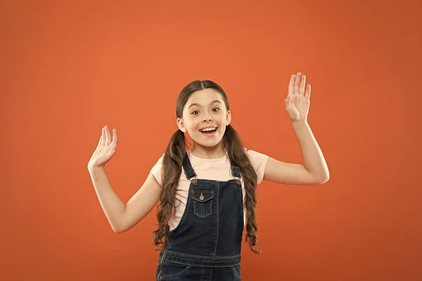 Pareces feliz e entusiasmada. Menina feliz com sorriso bonito no fundo laranja. Criança pequena alegre feliz sorrindo com aparência de moda. Criança adorável desfrutando de infância feliz — Fotografia de Stock