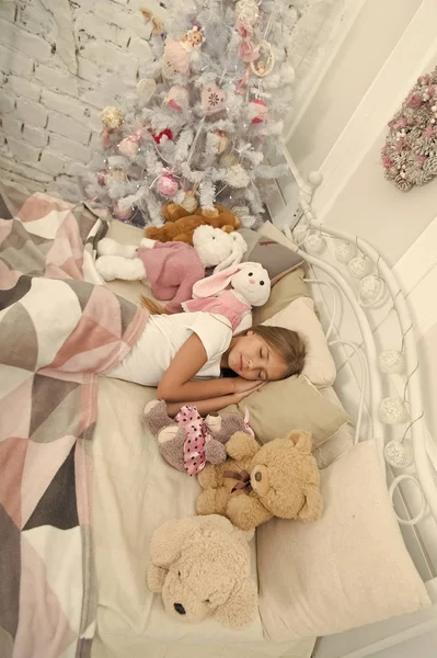 Tranquilo y tranquilo. Niña acostada en la cama con juguetes. Linda chica se durmió después de la noche de Navidad. Niña dormida. Un niño duerme en el árbol de Navidad. Sueño tranquilo y descanso en las vacaciones de invierno —  Fotos de Stock