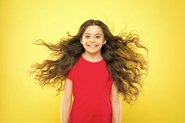 J'ai juste lâché mes cheveux. Enfant heureux avec des cheveux coulants sur fond jaune. Petit enfant avec un sourire mignon et des cheveux ondulés texturés. Adorable petite fille souriant avec de longs cheveux bruns — Photo