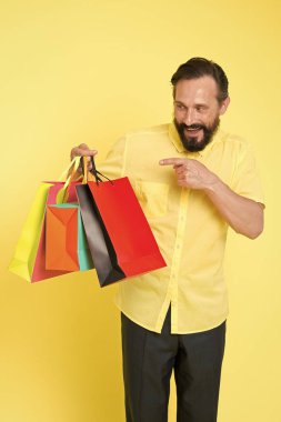 Alışveriş mutluluğu. Alışverişten zevk alan bir adam. Sarı arka planda alışveriş torbası olan sakallı olgun bir adam. İndirim ve indirim. İnternetten alışveriş. Kârlı bir alışveriş. Tezgahtar veya satış uzmanı