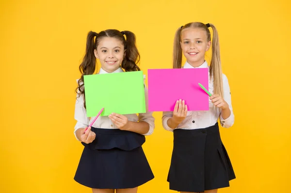 Tillbaka till skol reklamen. Glada skolbarn som pekar på tomma ark på gul bakgrund. Små barn börjar nytt läsår. Små flickor som håller tomma skol affischer för text, kopiera utrymme — Stockfoto