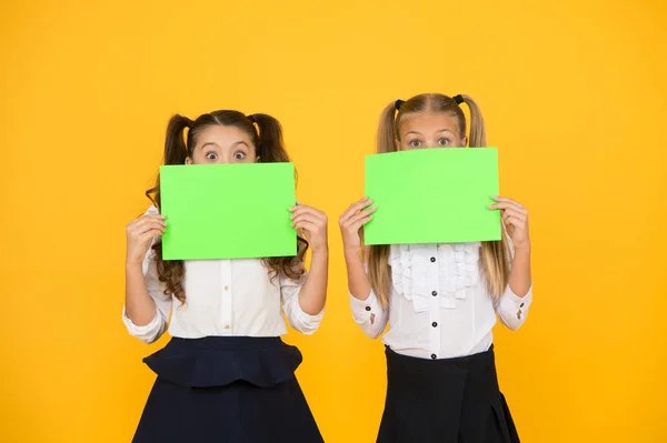 No proszę. Dziewczynki trzymające puste kartki papieru na żółtym tle. Małe dzieci z pustym zielonym papierem szkolnym do zadań lub prac projektowych. Papiery egzaminacyjne. Papier akademicki, przestrzeń do kopiowania — Zdjęcie stockowe