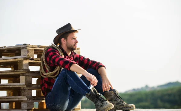 Mirando el atardecer. Cowboy granjero hombre guapo relajarse después de un duro día de trabajo en el rancho. Romanticismo de la cultura occidental. Granjero en sombrero sentarse relajarse. Agricultor disfrutar de la vista desde su granja. Humor pacífico —  Fotos de Stock