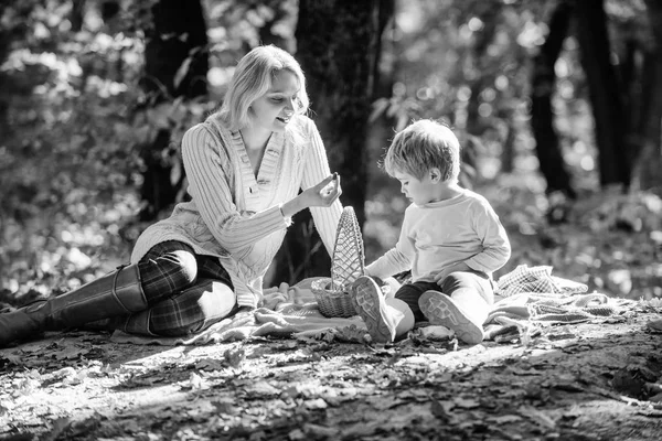 Family picnic. Mother pretty woman and little son sit on plaid relaxing forest picnic. Good day for spring picnic in nature. Explore nature together. Mom and kid boy relaxing while hiking in forest