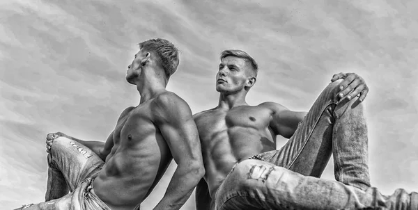 Homens gêmeos irmãos musculosos caras sentar relaxar céu fundo. Homens atleta muscular forte fisiculturista relaxante. Beleza divina. Torso sexy corpo atraente. Calça jeans enfatizar a sexualidade masculinidade — Fotografia de Stock