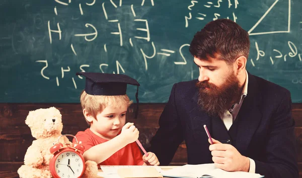 Hometask kavramı. Baba ev işini kontrol ediyor, oğlana yardım ediyor, evlat. Öğretmenle okuyan hevesli bir çocuk. Sınıfta resmi giyim öğretmeni ve harç tahtasında öğrenci, backgroun üzerinde tebeşir tahtası