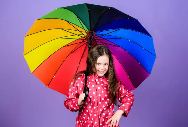 Бути веселкою в деяких хмарах. Дощовий день весело. Щаслива прогулянка під парасолькою. Насолоджуйтесь концепцією дощу. Дівчинка щаслива тримає барвисту парасольку веселки. Дощова погода з належним одягом. Яскрава парасолька — стокове фото