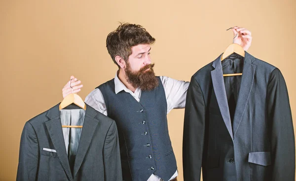 Siguiendo elegante estilo mens. Hombre barbudo sosteniendo chaquetas para hombre en los grandes almacenes. Hipster elegir chaqueta de traje en mens boutique. Empresario haciendo formal la elección de ropa para hombre en el armario — Foto de Stock