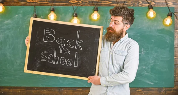 Professeur de lunettes tient tableau noir avec titre de retour à l'école. Éducation et concept d'étude. Homme à la barbe et la moustache sur le visage calme accueille les étudiants, tableau sur backgroun — Photo