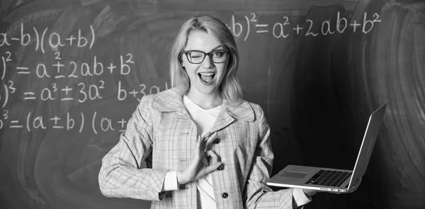 Online schooling concept. Woman wear eyeglasses holds laptop surfing internet. Educational site for teachers. Educator smart clever lady with modern laptop searching information chalkboard background Stock Photo