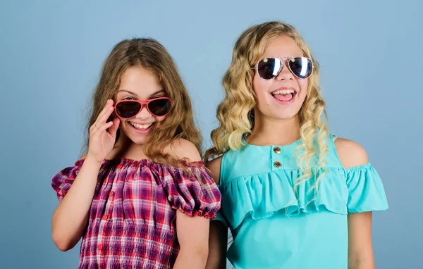 Fashionista. Kid zomer mode. kapsalon. schoonheid en mode. lang blond krullend haar. vrolijke kleine meisjes in zonnebrillen. trendy zusters. Vriendschap. Gelukkig kleine meisjes met lang gezond haar — Stockfoto