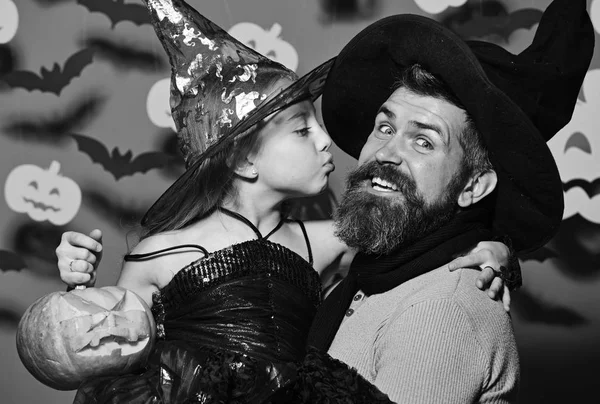 Wizard and little witch in black hats hold pumpkin