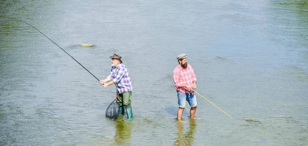 Pescador feliz com vara de pesca e rede. Atividades hoteleiras e desportivas. A pescar juntos. Os homens estão na água. A pesca é muito mais do que o peixe. Amizade masculina. Pescando pai e filho. Fim de semana — Fotografia de Stock