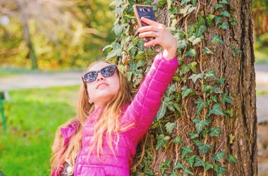 parkta mutlu çocuk. selfie zamanı. Doğal güzellik. Çocukluk mutluluğu. yaz doğa. küçük kız parkta selfie yapmak. Bahar tatili. Yeşil çevre. sarmaşık yaprakları ile ağaç üzerinde tırmanma bitki