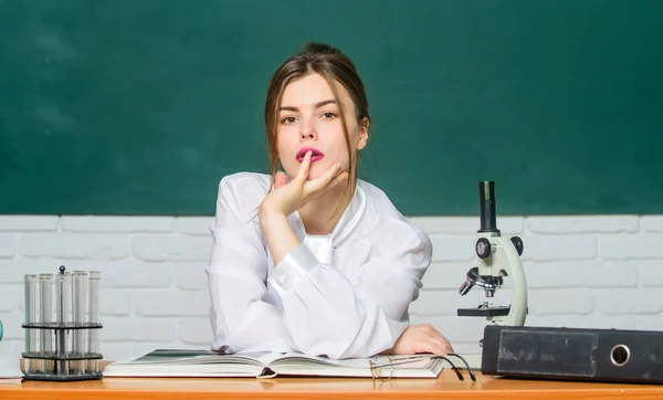 生物学の学生は教室の黒板の背景に座ります。女性かなり愛らしい教師や学生。顕微鏡で化学生物学者。賢い学生だ一生懸命勉強してください。科学的研究教育の概念 — ストック写真