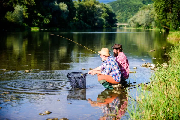 Condividere i suoi segreti. Esperto pescatore mostra consigli al figlio. Trasferire conoscenza. Uomini che pescano pesci lungo il fiume. Insegnare pesca. Gli amici passano un bel po 'di tempo sul lungofiume. Bella serata lungo il fiume — Foto Stock