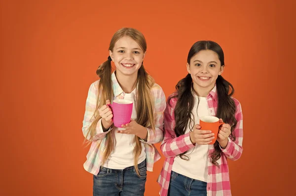 Убедись, что дети пьют достаточно воды. Девочки держат чашки оранжевый фон. Сестры держат кружки. Пью чай во время перерыва. Расслабляюсь выпивкой. Перерыв на чай. Дети не пьют достаточно в течение учебного дня — стоковое фото