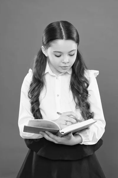 Estudante escrevendo notas sobre fundo laranja. lição de leitura. obter informações livro de formulário. de volta à escola. criancinha concentrada no trabalho. menina pequena em uniforme escolar. escrita na pasta de trabalho — Fotografia de Stock