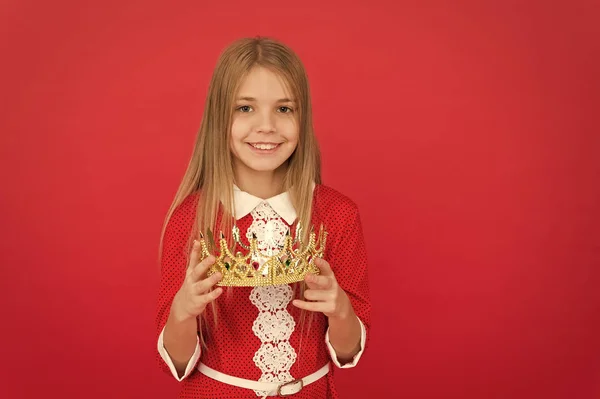 Lady little princess. Girl cute smile hold crown while stand red background. Best award for me. Kid hold golden crown symbol of princess. Happy childhood concept. Every girl dreaming become princess