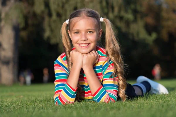 Vidám iskoláslány a napsütéses napon. Lány Ponytails frizuráját élvezni pihenni. Élet boldog élet. Boldog mosolygó tanuló. jó szórakozást. Lány gyerek szóló zöld fű. Egészséges érzelmi boldog gyerek pihentető szabadban — Stock Fotó