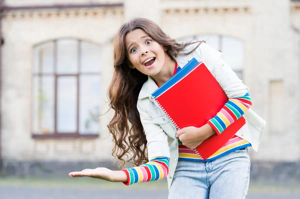 Produktwerbung. glückliches kleines Schulkind, das sein Produkt präsentiert. kleines Mädchen mit Büchern, die lächeln und Produkte oder Dienstleistungen präsentieren. Sie können mit diesem Produkt nie etwas falsch machen — Stockfoto