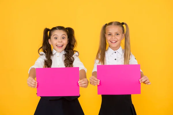 Promoot met advertenties. Gelukkige kleine kinderen tonen roze papieren vellen voor reclame op gele achtergrond. Klein meisje reclame product of evenement. Reclame en marketing, kopieer ruimte — Stockfoto
