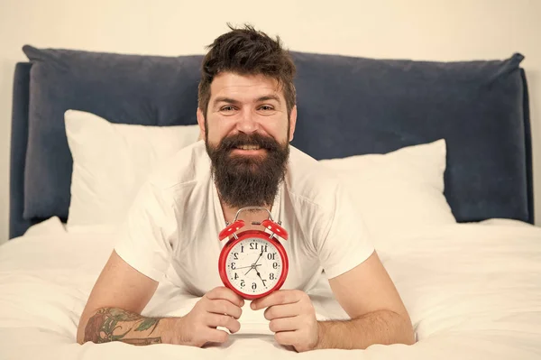 Pourquoi vous devriez vous réveiller tôt chaque matin. Avantages pour la santé de se lever tôt. Se lever tôt donne plus de temps pour se préparer et être en temps opportun. Hipster barbu homme couché dans le lit avec réveil. Il est temps de se réveiller — Photo