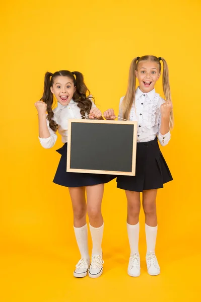 Schrijven is cool. Gelukkige kleine meisjes houden zwart schrijfoppervlak op gele achtergrond. Kleine kinderen gebaren met schoolbord voor het schrijven van informatie. Blanco bord voorschrijven, ruimte kopiëren — Stockfoto