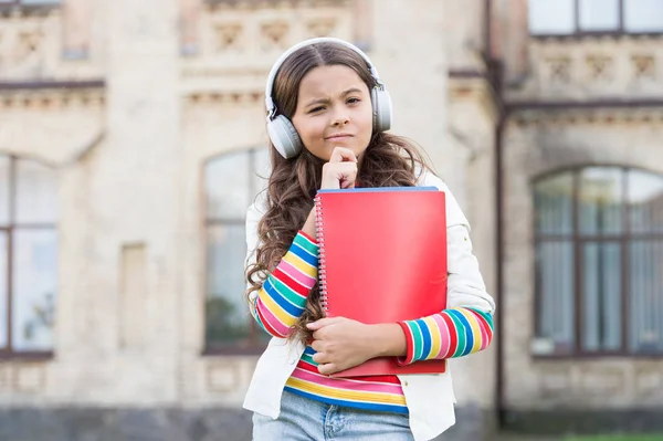 Entwicklung effektiver Hörfähigkeiten. Seriöses kleines Mädchen hört Audio-Unterricht über Kopfhörer. Niedliches kleines Kind übt das Hörverstehen. Notizen machen, während man zuhört, um Vokabeln zu behalten — Stockfoto