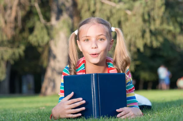 Urocza książkowy robak. Czas szkolny. Rozwijanie troskliwych uczących się, którzy aktywnie rosną i osiągają. Małe dziecko czytanie książki. Uczennica czytanie historie relaksujący zielony trawnik. Cute uczeń cieszyć czytania — Zdjęcie stockowe